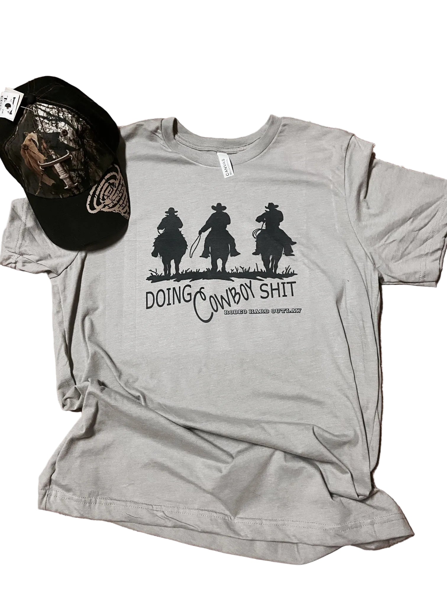 Gray t-shirt with graphic design and text, accompanied by a black cap on a textured surface.